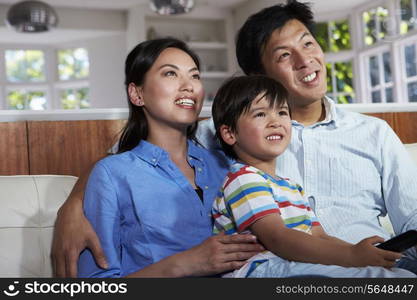 Asian Family Sitting On Sofa Watching TV Together