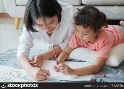 Asian family with mother and daughters are drawing on paper at home. Parents are teaching girl to draw with colors on white paper. Self Study concept at home