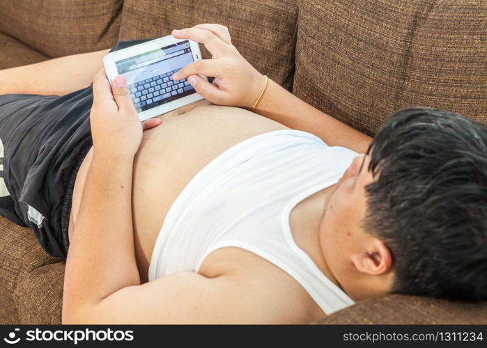 Asian fat man Relaxing in the sofa with the tablet at home