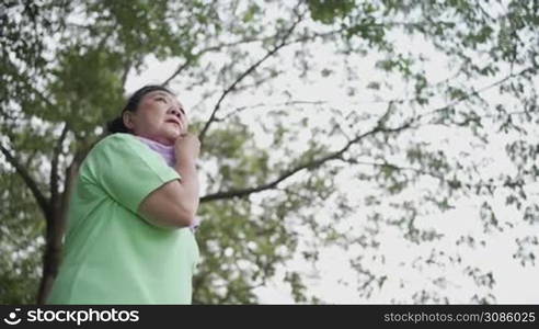 Asian fat Senior female wipe sweat during exercise at the park, standing outdoors and rest after exercising, retirement life, resting after work out, health caution, women breast cancer risk