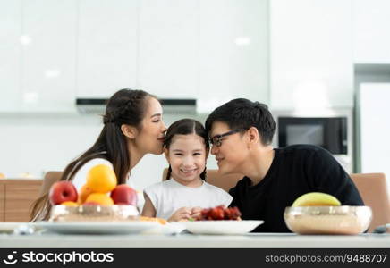 Asian father and mother Show your love to little daughter and having breakfast together happily in the dining room of the house.