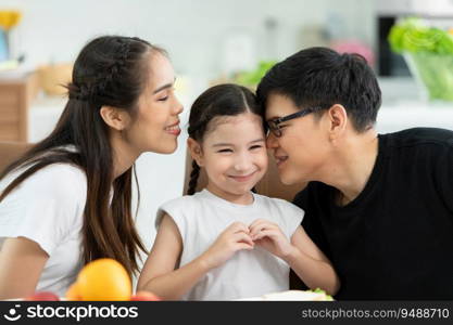 Asian father and mother Show your love to little daughter and having breakfast together happily in the dining room of the house.