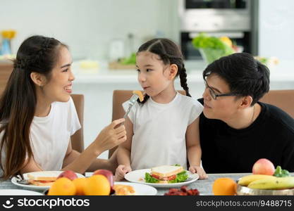 Asian father and mother Show your love to little daughter and having breakfast together happily in the dining room of the house.