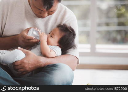 Asian father holding and feeding her baby boy with milk from baby bottle.