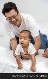 Asian father touching and playing with the boy baby on the bed in the house, Family Lifestyle Concept