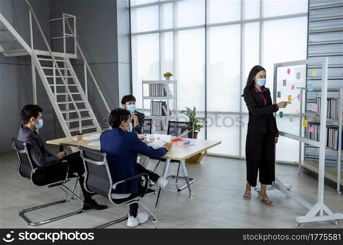asian female coach Wear protective mask speaker make flip chart presentation to diverse business people meeting with diverse genders (LGBT) in the room at office,COVID-19