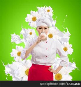 Asian female cook against milk splashes. Asian female cook against milk splashes in red apron against flower background drinking milk