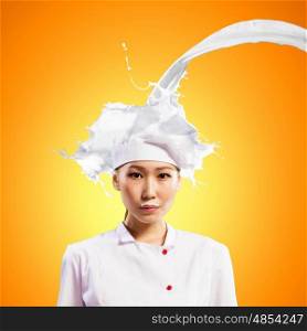 Asian female cook against milk splashes. Asian female cook standing against milk splashes in red apron against colo?? background