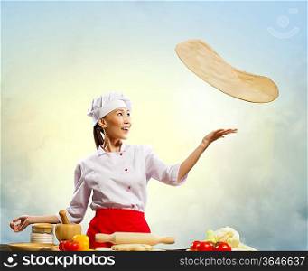 Asian female cook making pizza standing against color background