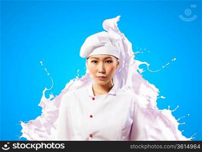 Asian female cook standing against milk splashes in red apron against colo: background