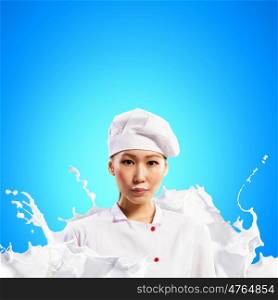 Asian female cook standing against milk splashes in red apron against colo? background