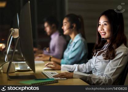 Asian Female customer care service with business man smiling and working hard late in night shift at office,call center department,worker and overtime,teamwork with colleagues for success