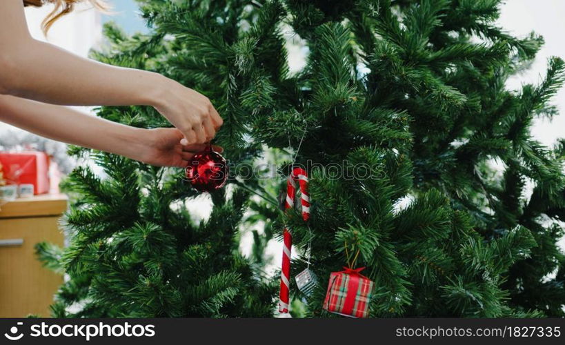 Asian female decorated with ornament on Christmas tree at Christmas and New Year festival at home. Xmas celebration event preparation or winter holidays festival indoor party concept. Close up shot.