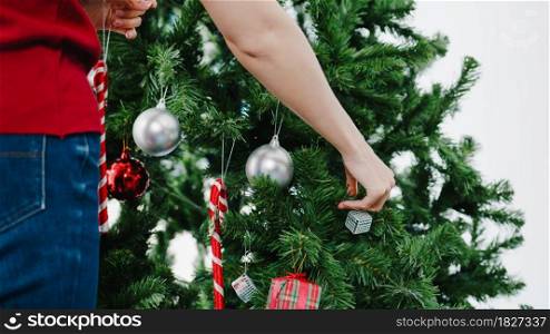 Asian female decorated with ornament on Christmas tree at Christmas and New Year festival at home. Xmas celebration event preparation or winter holidays festival indoor party concept. Close up shot.