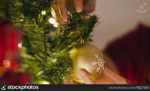 Asian female decorated with ornament on Christmas tree at Christmas night and New Year festival at home. Xmas celebration event preparation or winter holidays festival indoor party. Close up shot.