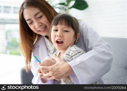 Asian female dentist teaching cute little girl brushing teeth with toothbrush and stomatologist telling girl child about oral hygiene in dental clinic, Education and prevention cavities concept.