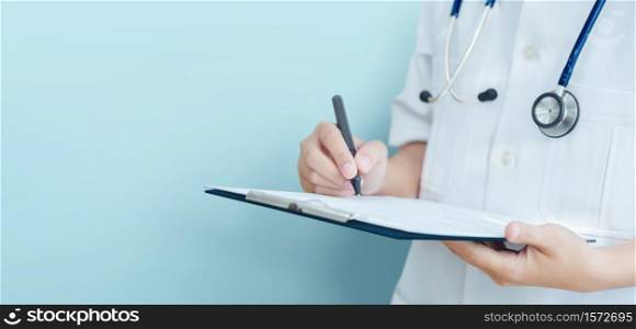Asian female Doctor hand taking note information of patient in paperwork checklist on clipboard with blue background, isolated, banner.