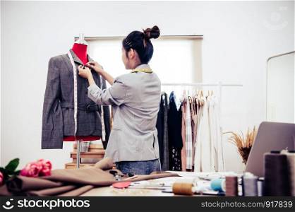 Asian female fashion designer girl making fit on the formal suit uniform clothes on mannequin model. Fashion designer stylish showroom. Sewing and tailor concept. Creative dressmaker stylist.