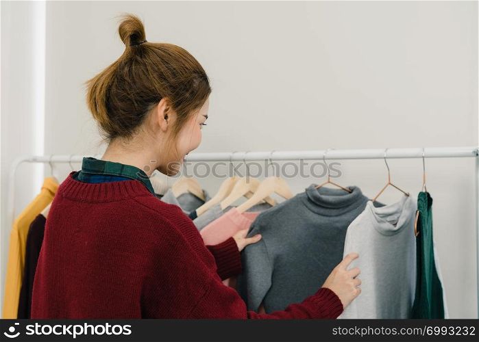Asian female fashion designer working, checking and choosing clothes design on clothes rack while working in the fashion studio. Lifestyle beautiful professional designer women working concept.