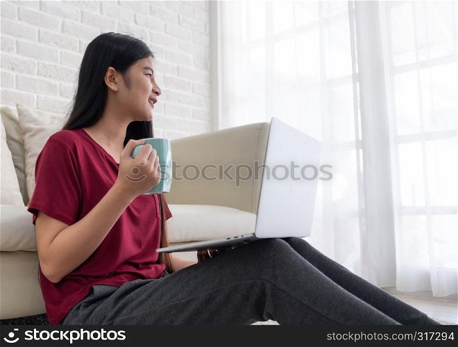 Asian female freelancer smile and drink coffee with relax emotion and looking out of window at home.working online lifestyle