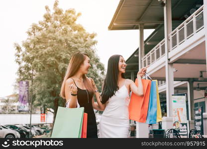 Asian female friends holding shopping bag and walking outside the mall.