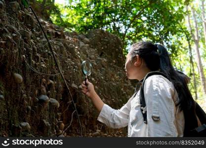 Asian female geologist researcher analyzing rocks with a magnifying glass in Mae Wang Nature Park, Thailand. Exploration Geologist in the Field