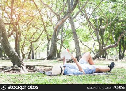 Asian female in blue jeans lying down and reading a book in park, Lifestyle people, Happy moment
