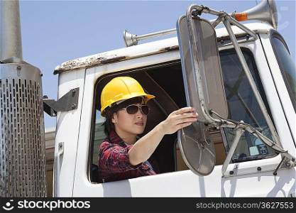 Asian female industrial worker adjusting mirror while sitting in logging truck