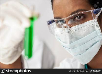 Asian female medical or scientific researcher or doctor looking at a test tube of green solution in a lab or laboratory