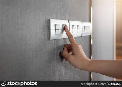 Asian female right hand is turning on or off on grey light switch over textile texture wall. Copy space.