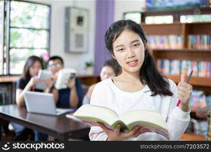 Asian female students holding for selection Book in library