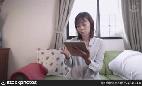 Asian female use laplet sitting on sofa inside home living room, weekend leisure activity, working from home, network connection online shopping service, touch screen device, digital marketing