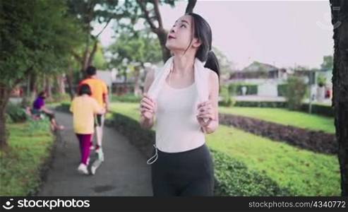 Asian female wear sport clothing enjoy walking inside the public park, cardio exercise training, family in the park on background positive energy, listening to music, positive emotion smiling face