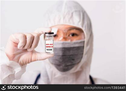 "Asian female woman doctor or nurse in PPE uniform and gloves wearing face mask protective in laboratory holding medicine vial coronavirus vaccine bottle and on bottle has "COVID-19 VACCINE" text label"