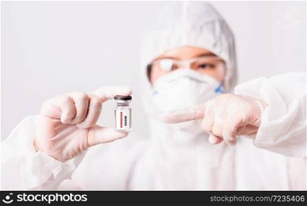"Asian female woman doctor or nurse in PPE uniform and gloves wearing face mask protective in laboratory point medicine vial coronavirus vaccine bottle and on bottle has "COVID-19 VACCINE" text label"