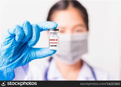 "Asian female woman doctor or nurse in uniform and gloves wearing face mask protective in laboratory holding vial corona vaccine bottle on hand and bottle have "COVID-19 CORONAVIRUS VACCINE" text label"
