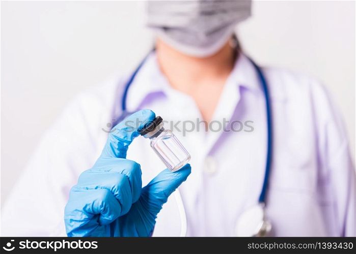 Asian female woman doctor or nurse in uniform with stethoscope wearing face mask protective in laboratory looking medicine vial vaccine bottle on hand holding, studio shot, Health medical concepts