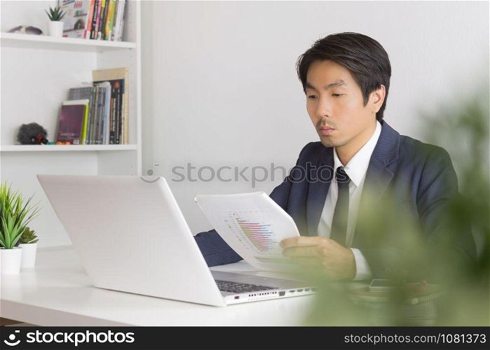 Asian Financial Advisor or Asian Consulting Businessman Analyze Financial Report in front of Laptop. Asian financial advisor or Asian consulting businessman working in office