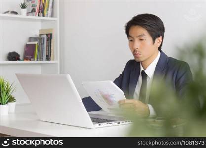 Asian Financial Advisor or Asian Consulting Businessman Analyze Financial Report in front of Laptop. Asian financial advisor or Asian consulting businessman working in office