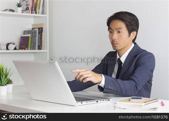 Asian Financial Advisor or Asian Consulting Businessman in Suit Recommend Customer Via Internet in Office. Asian financial advisor or Asian consulting businessman pointing laptop monitor