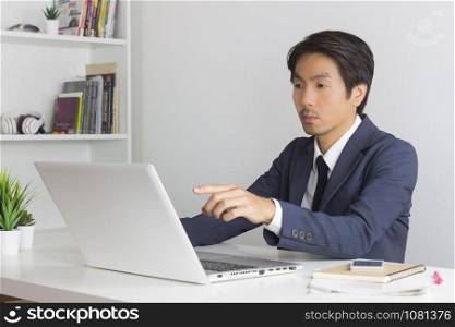 Asian Financial Advisor or Asian Consulting Businessman in Suit Recommend Customer Via Internet in Office. Asian financial advisor or Asian consulting businessman pointing laptop monitor
