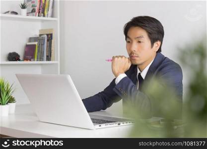 Asian Financial Advisor or Asian Consulting Businessman in Suit Seriously Thinking in front of Laptop. Asian financial advisor or Asian consulting businessman contact with customer via internet