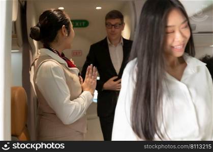 Asian flight attendant greeting passengers walking and leaving plane. Cabin crew or air hostess working in airplane.