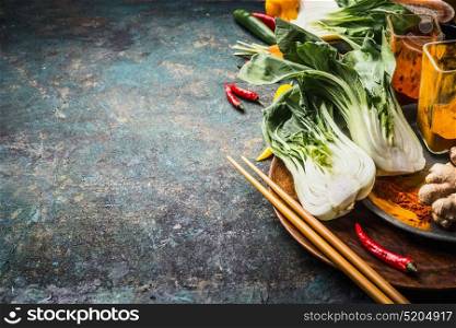 Asian food and eating concept: Chinese or Thai cuisine, cooking ingredients with pak choi and chopsticks on dark vintage background, place for text
