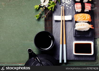 Asian food background (black iron tea set and sushi on rustic table)