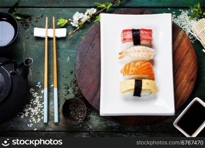 Asian food background (black iron tea set and sushi on rustic table)