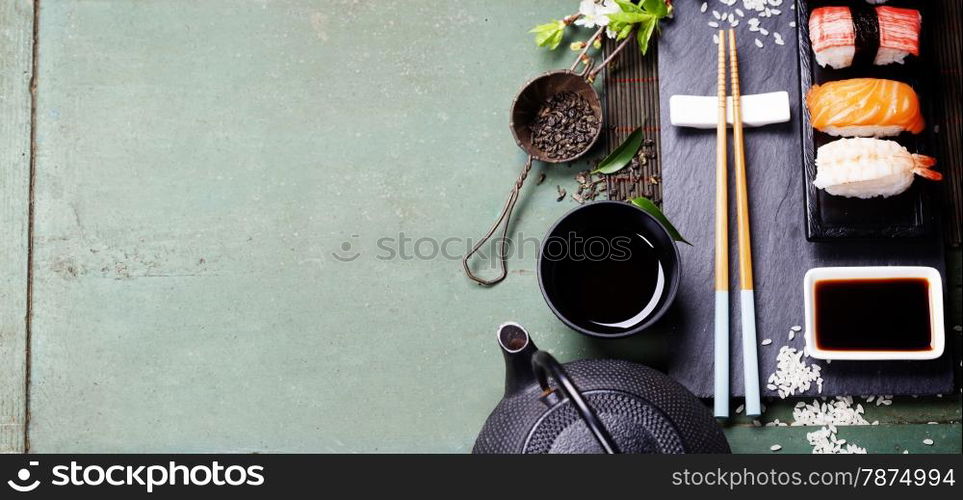 Asian food background (black iron tea set and sushi on rustic table)