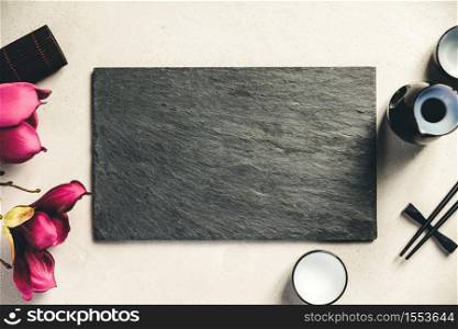 Asian food background - sake and chopsticks on a slate board over grey concrete background. Top view, flat lay. Asian food background - sake and chopsticks on a slate board over grey concrete background. Top view