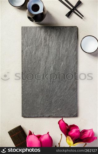 Asian food background - sake and chopsticks on a slate board over grey concrete background. Top view, flat lay. Asian food background, top view, flat lay