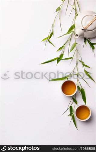 Asian food background set with green tea, cups and teapot with bamboo branches and free space for text on white background. Flat lay